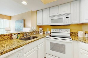 A kitchen with white cabinets, a granite countertop, a built-in microwave, and a stove. - Carolinian Beach Resort 1935 (Myrtle Beach)