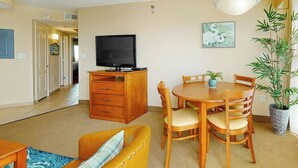 Ett vardagsrum med en tv, ett matbord i trä, stolar, en soffa och en krukväxt.
