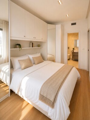 Ein modernes Schlafzimmer mit einem großen Bett, integrierten Stauraumlösungen und einem durch eine offene Tür einsehbaren Badezimmer.