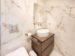 Ein modernes Badezimmer mit Marmorwand, einem runden Waschbecken, einem Spiegel, einer Toilette und einem Schrank.