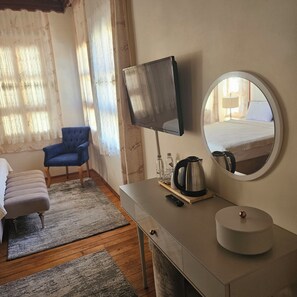 Une chambre d’hôtel avec un lit, un fauteuil bleu, une télévision, une bouilloire et une table de chevet.