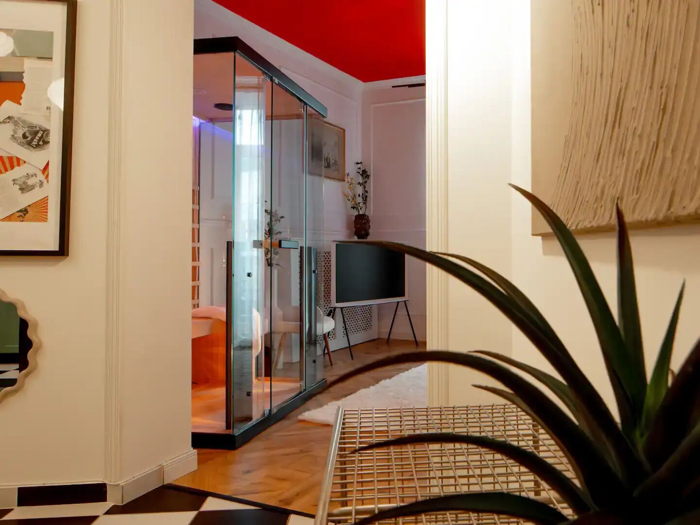 Ein modernes Interieur mit einer Glastür zu einem Badezimmer, einem kleinen Tisch mit einer Vase und einer Pflanze im Vordergrund.