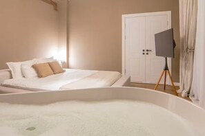 A bedroom with a bed, a large window, a white door, and a television on a stand. - Calea Victoriei Luxury Suite Bedroom Tub (București)