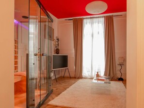Ein modernes Wohnzimmer mit Glastrennwand, Flachbildfernseher, weißem Teppich und roter Decke.