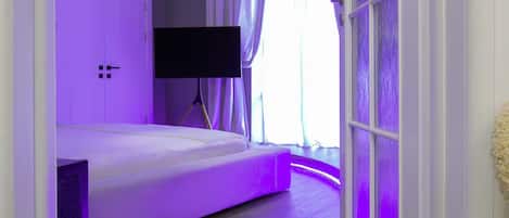 Een slaapkamer met een bed, een televisie en een raam met gordijnen.