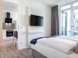 Quarto de hotel moderno com uma cama, televisão na parede, cozinha compacta e uma janela grande.