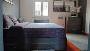 A bedroom with a bed, a dresser, a radiator, and a window.