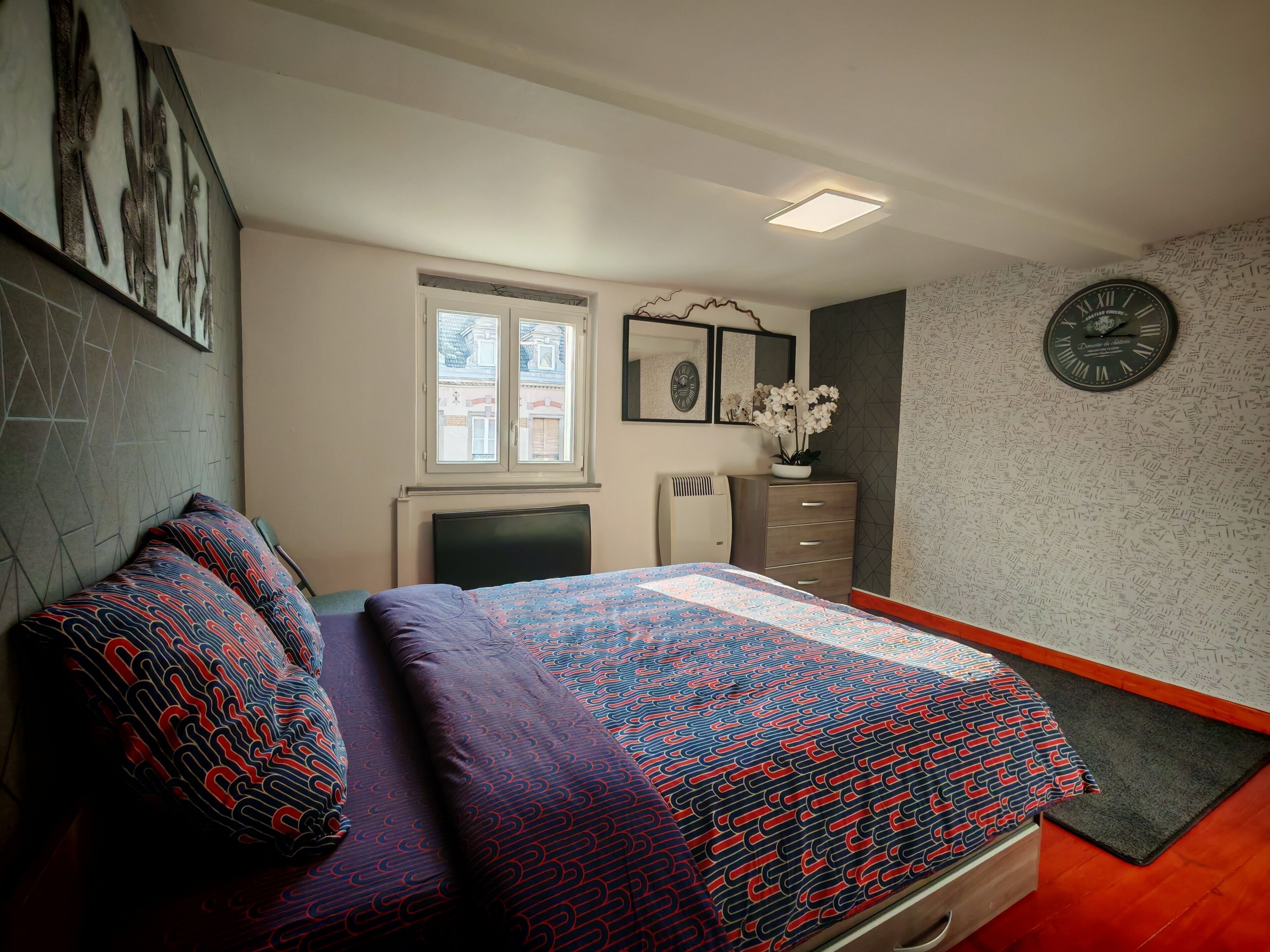 A bedroom with a bed, a dresser, a clock, and a window.