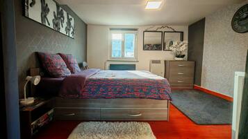 A bedroom with a bed, a dresser, a nightstand, a window, and a clock on the wall.