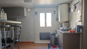 A kitchen with a bar stool, a trash bin, and a window.