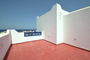 Eine Dachterrasse mit roten Fliesen, weißen Wänden und einem blauen Geländer.