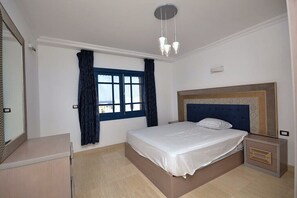 Ein Schlafzimmer mit Bett, Nachttisch, Spiegel, Fenster mit Vorhängen und einer Deckenleuchte.