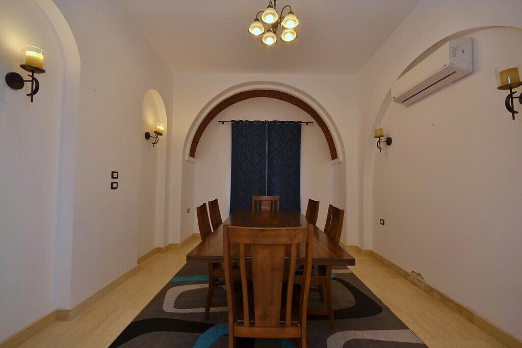 A dining area with a wooden table and chairs, an arched doorway, and wall-mounted lighting.