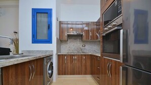 A kitchen with wooden cabinets, stainless steel appliances, and a blue-framed window. - Luxury 4-Bedroom Villa for Rent in Amaros. (Red Sea Governorate)
