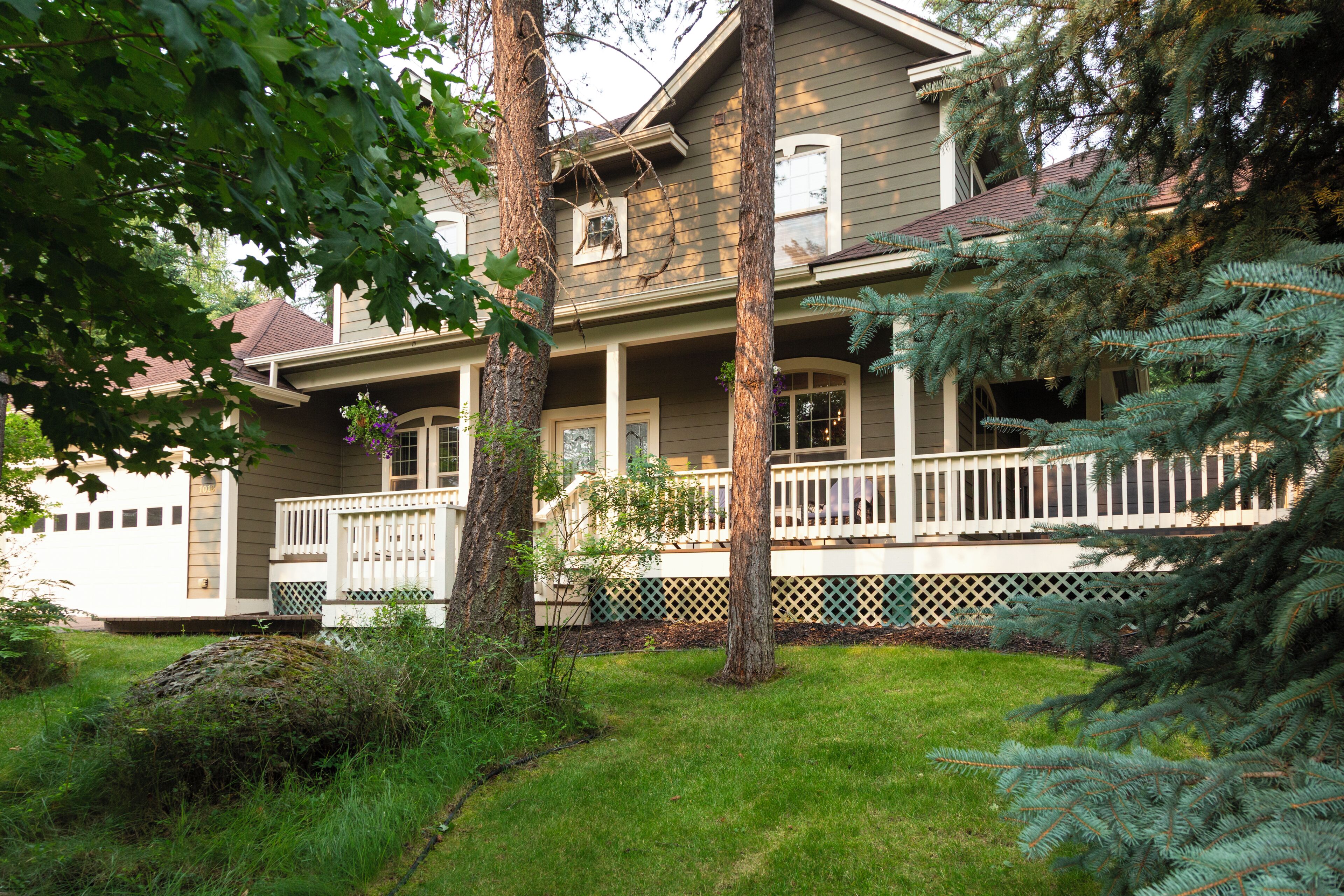A two-story house with a front porch, a covered entryway, and a small front yard with a tree and shrubbery.