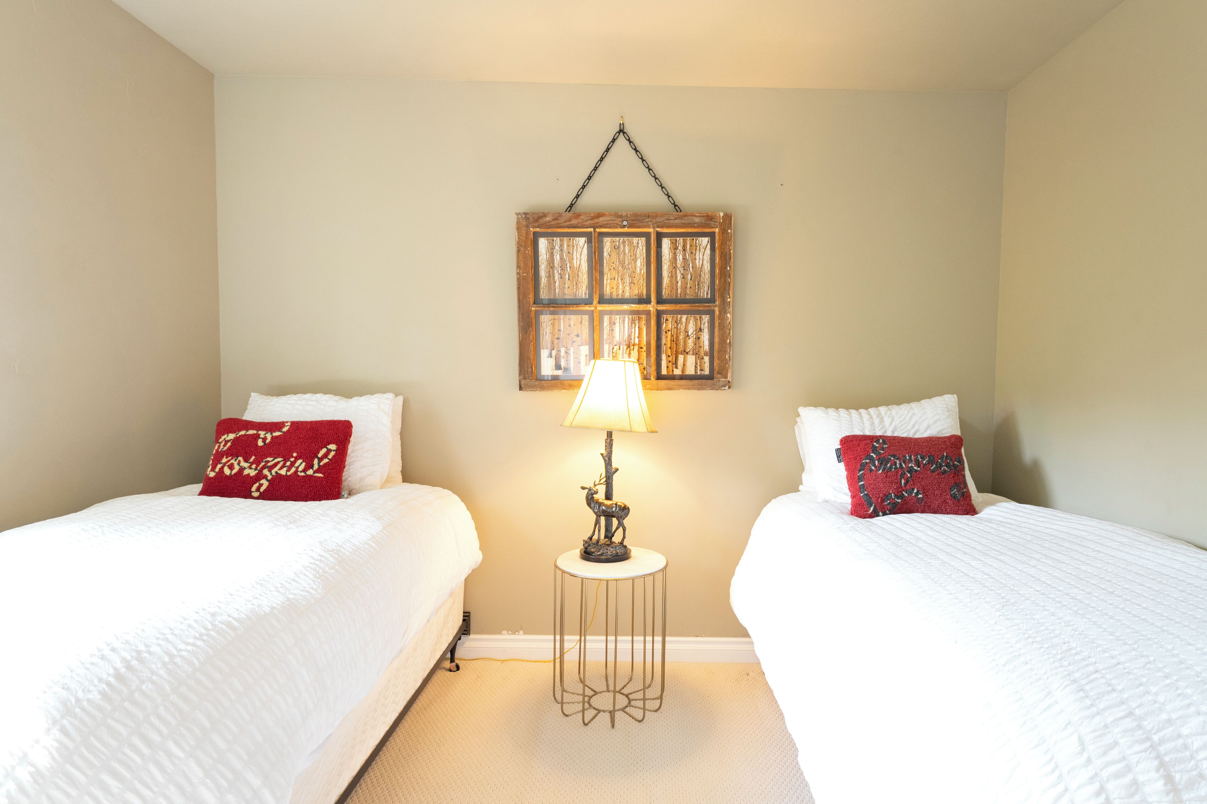 A hotel room with two beds, a bedside table with a lamp, and a wall-mounted picture frame.