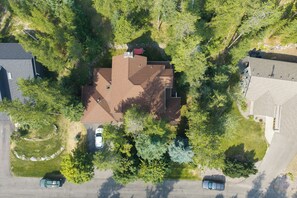Vue aérienne d’un quartier résidentiel, avec une maison dotée d’un toit en pente, entourée d’une végétation luxuriante et bordée d’autres propriétés.