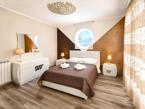 Ein modernes Schlafzimmer mit einem großen Bett, Nachttischen, einem Spiegel und Blick durch ein Fenster.