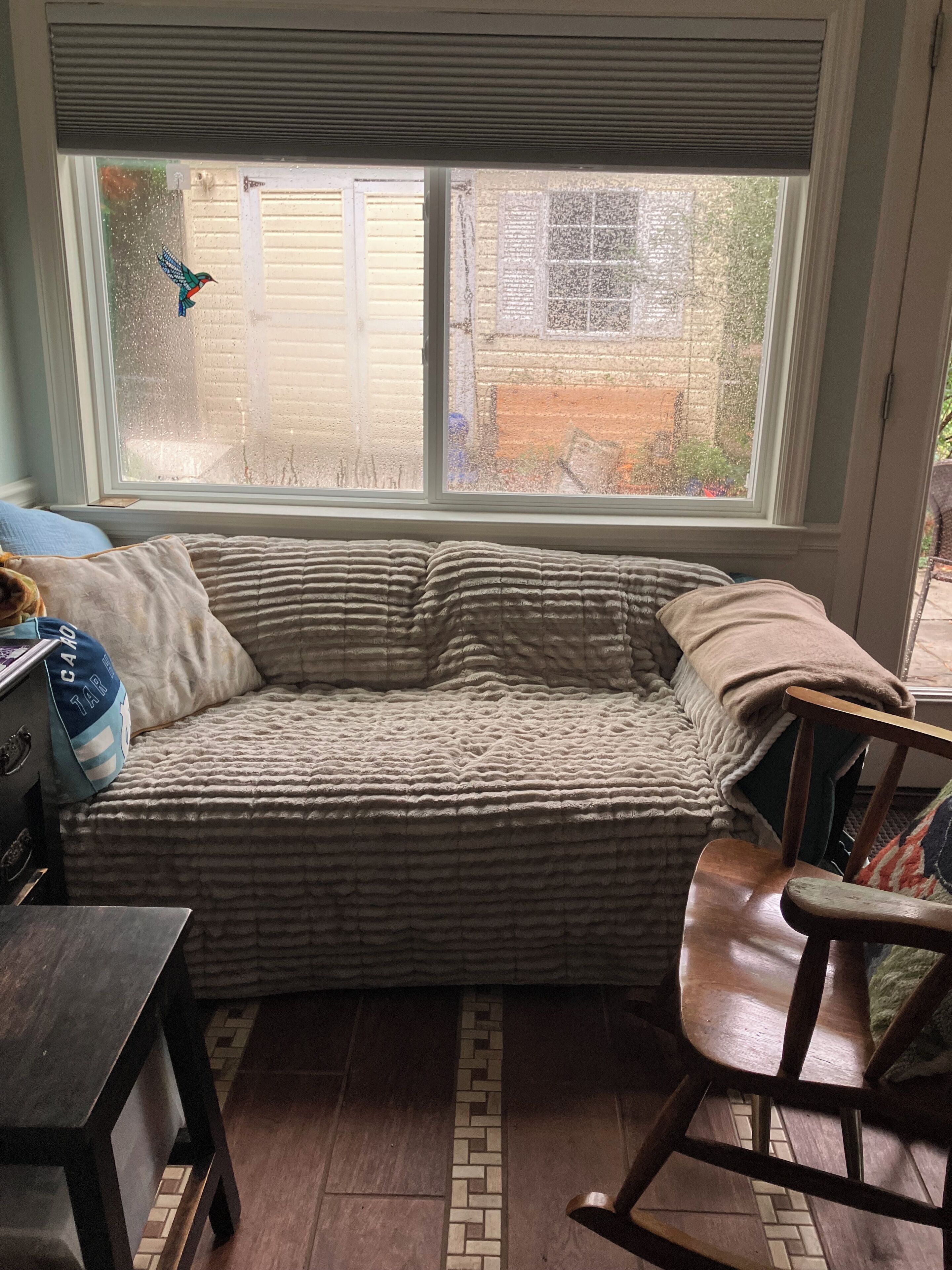Una habitación acogedora con ventanal, un banco acolchado, una mecedora y una mesita.