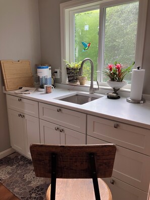A kitchen with a window, a sink, cabinets, a chair, a wooden cutting board, a coffee maker, a potted plant, and a tissue roll. - Charming 1-bedroom apartment with AC in vibrant Alexandria (Alexandria)
