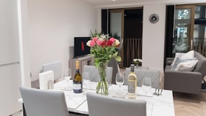 A modern dining area with a white table set for two, featuring a bottle of Prosecco and a bottle of Meiguan wine. - 1-Bed Flat 7 Min to Piccadilly Station (Manchester)