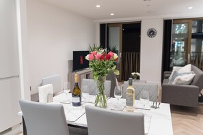 A modern dining area with a white table set for two, featuring a bottle of Prosecco and a bottle of Meiguan wine. - 1-Bed Flat 7 Min to Piccadilly Station (Manchester)