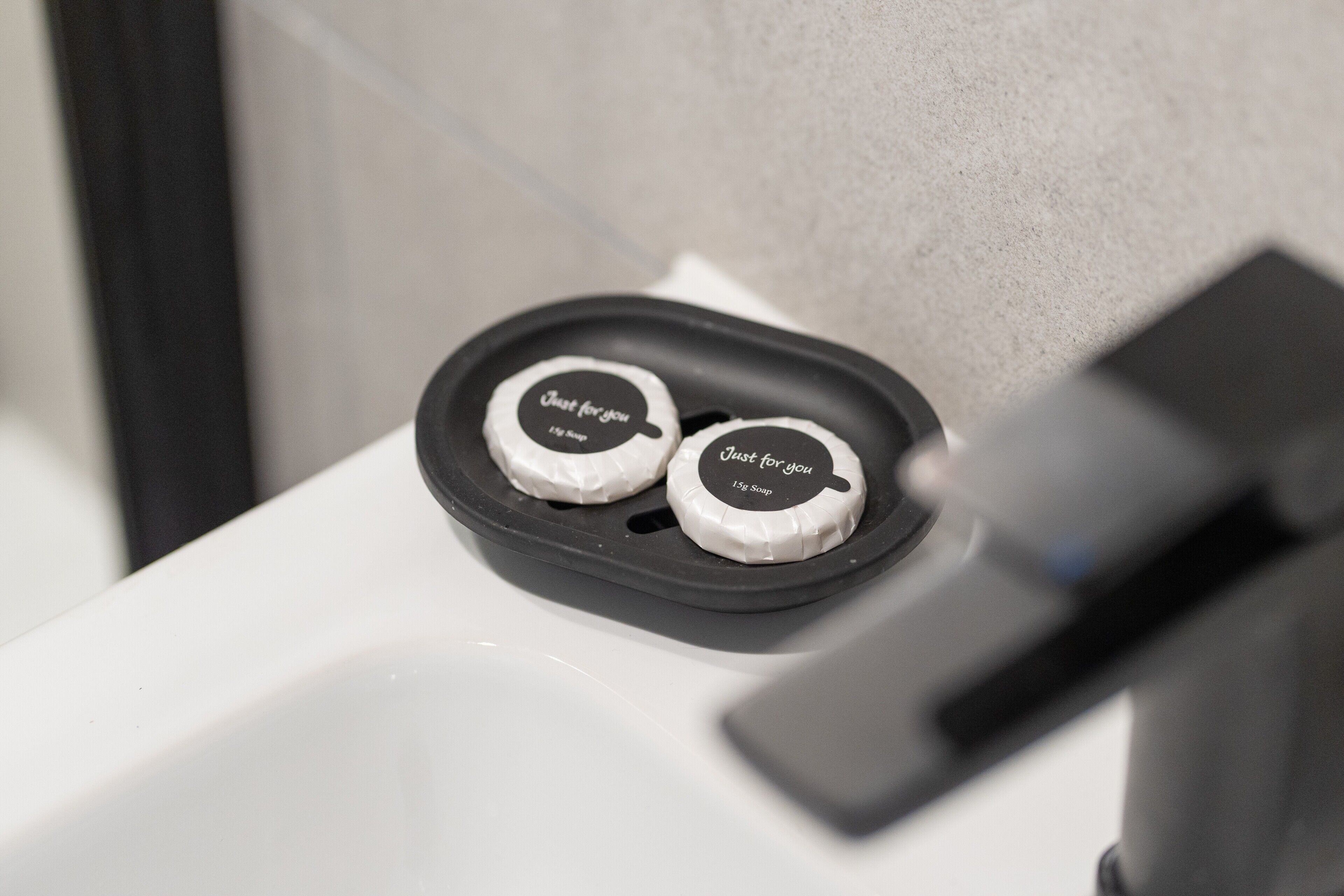 A bathroom sink with two soap dispensers labeled 'Just for you' and '1/2 Soap' on a black tray.