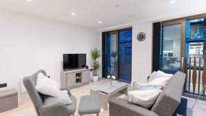 A modern living room with a flat-screen TV, grey upholstered chairs, a coffee table, and a potted plant. - 1-Bed Flat 7 Min to Piccadilly Station (Manchester)
