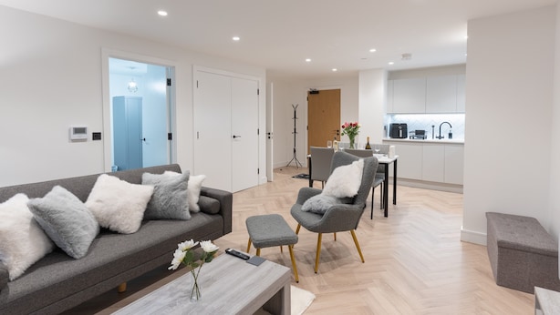 A modern living room with a grey sofa, a coffee table, and a dining area with a grey chair and table. - 1-Bed Flat 7 Min to Piccadilly Station (Manchester)