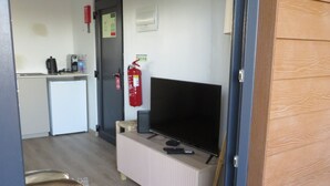 Ett rum med en tv på ett stativ, en brandsläckare på väggen och en liten köksdel.