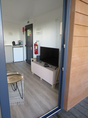 A room with a television on a stand, a fire extinguisher on the wall, and a small kitchenette area. - 1-Bedroom Bungalow (Ciborro)