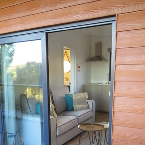 A modern interior with a glass door leading to a balcony, a sofa with cushions, and a small round table. - 1-Bedroom Bungalow (Ciborro)