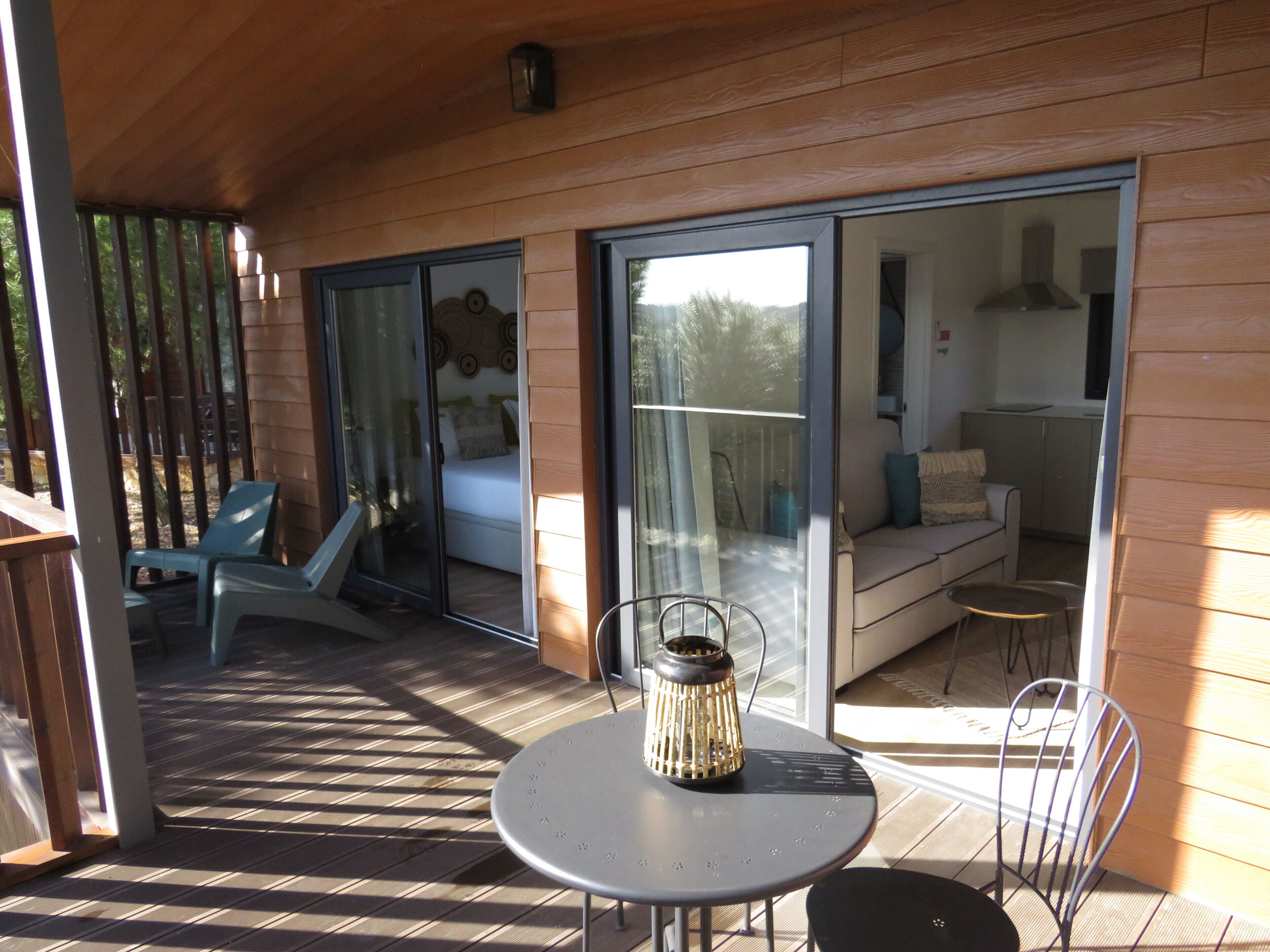 A covered outdoor area with a table and chairs, a sliding glass door leading to a living room, and a view of the outdoors.