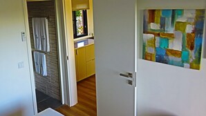 Ett rum med en vit dörr, ett badrum med en handduksställning och en färgstark, abstrakt målning på väggen.