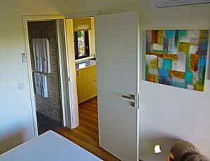 A room with a white door, a bathroom with a towel rack, and a colorful abstract painting on the wall. - 1-Bedroom Bungalow (Ciborro)