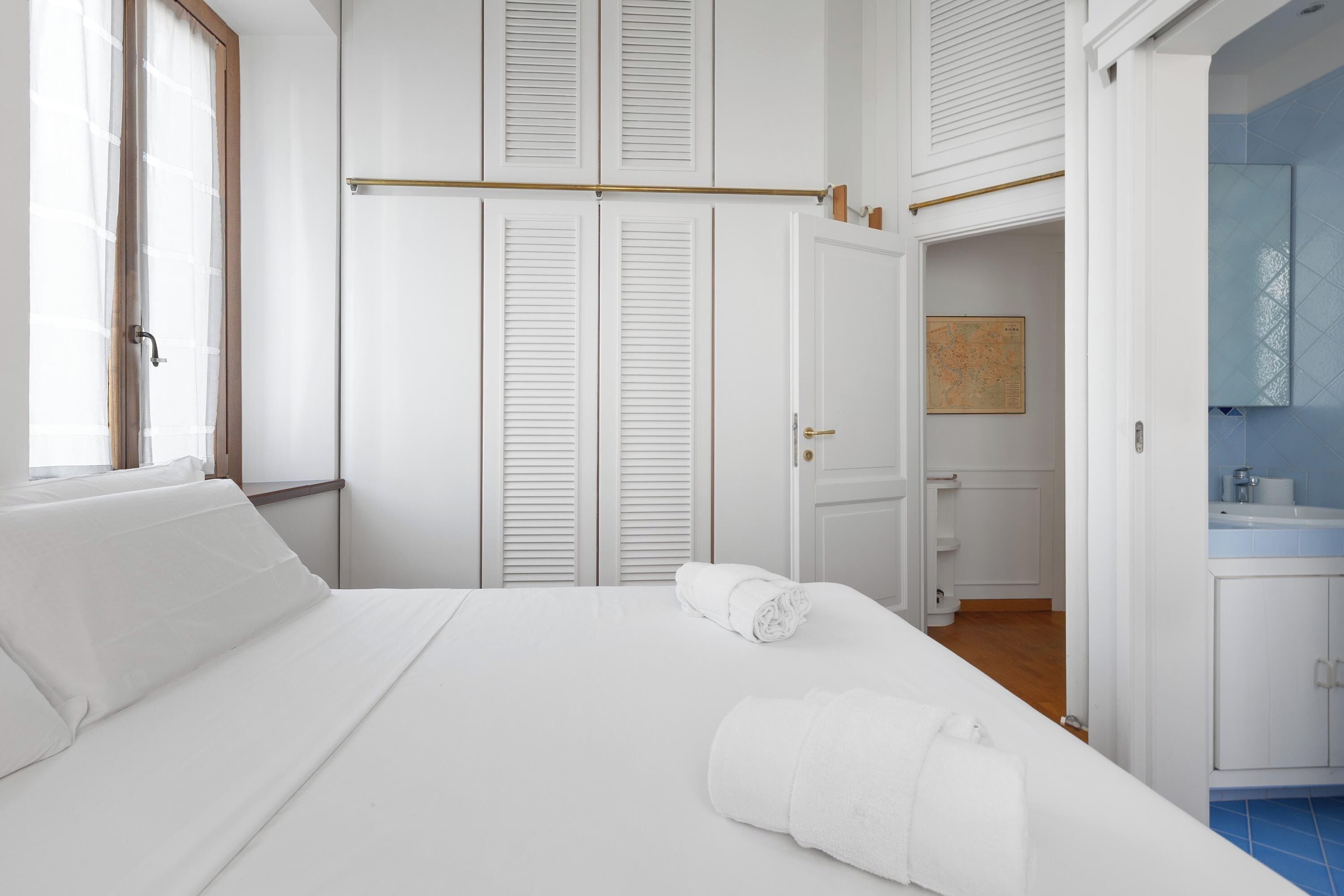 A hotel room with a bed, a window, a door, and a bathroom visible through an open door.
