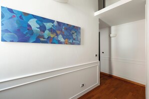 Ein Flur mit einem großen, abstrakten Gemälde an der Wand, weißen Wänden und Holzboden.
