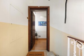 Ein Flur mit einer Holztür, einer Fußmatte, einem auf einem Ständer stehenden Laptop und einem Bild an der Wand.