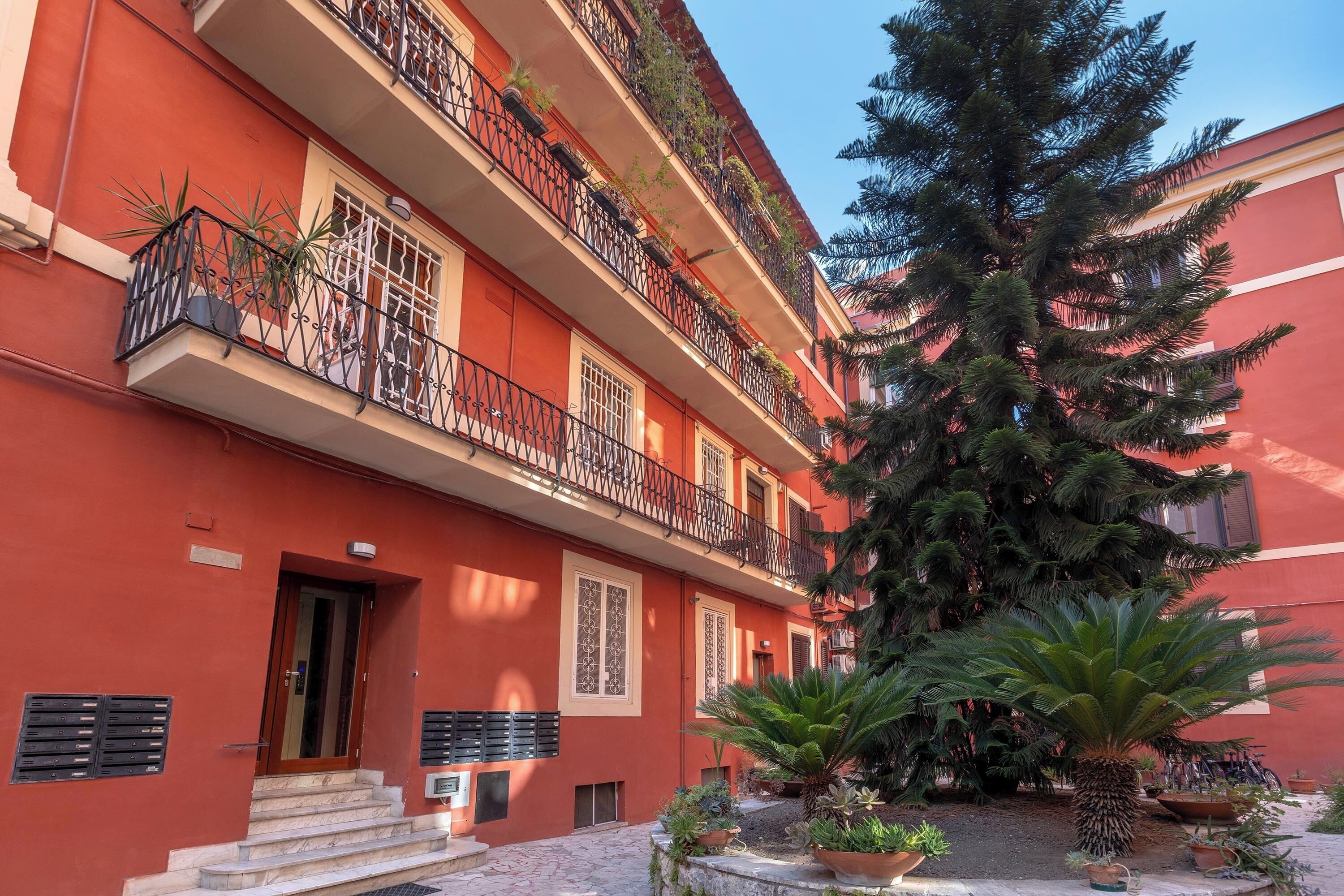 Un immeuble à plusieurs étages doté de balcons, d’un grand arbre et de plantes en pot.