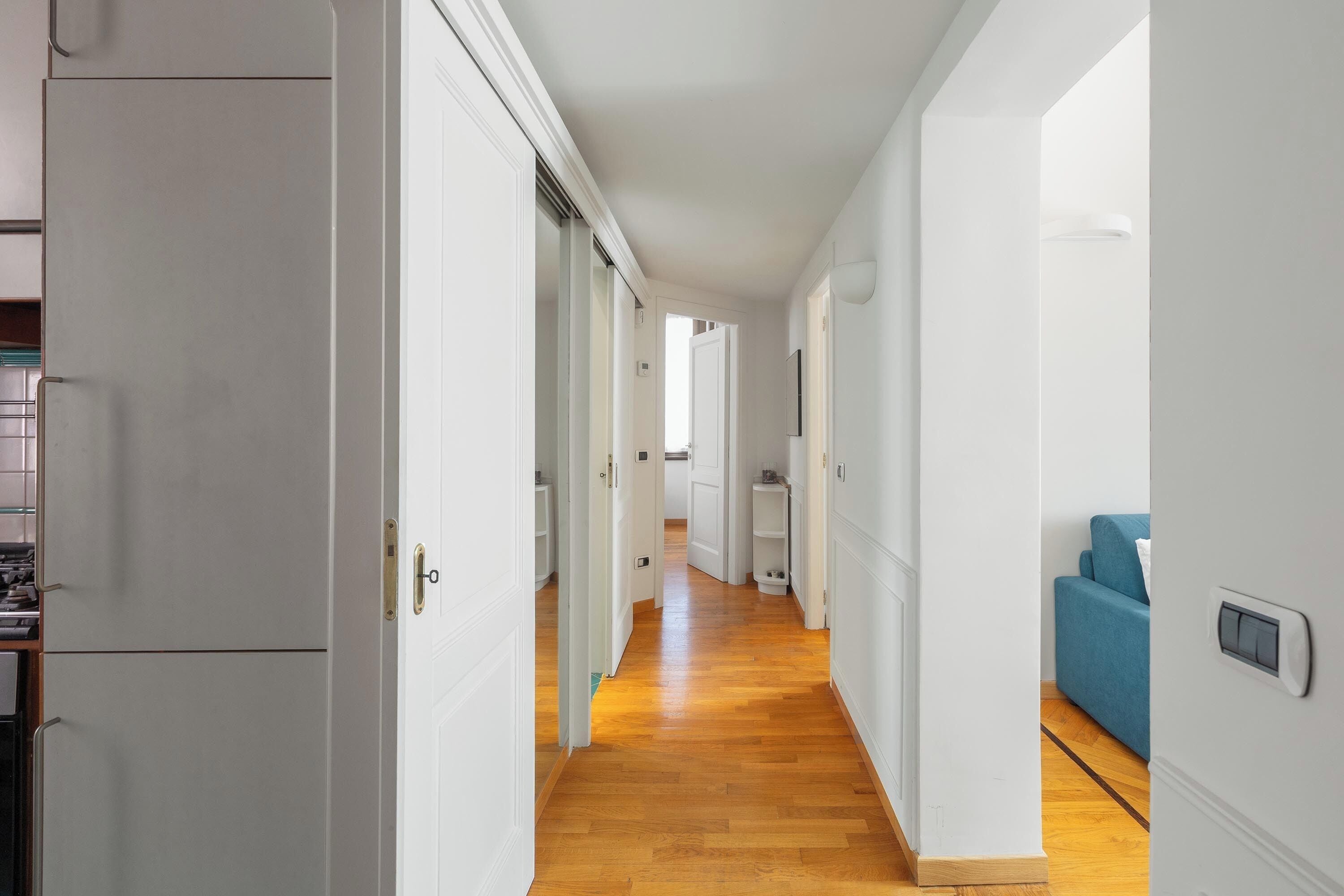 Un corridoio con pareti bianche, pavimento in legno e porte che conducono a diverse stanze.