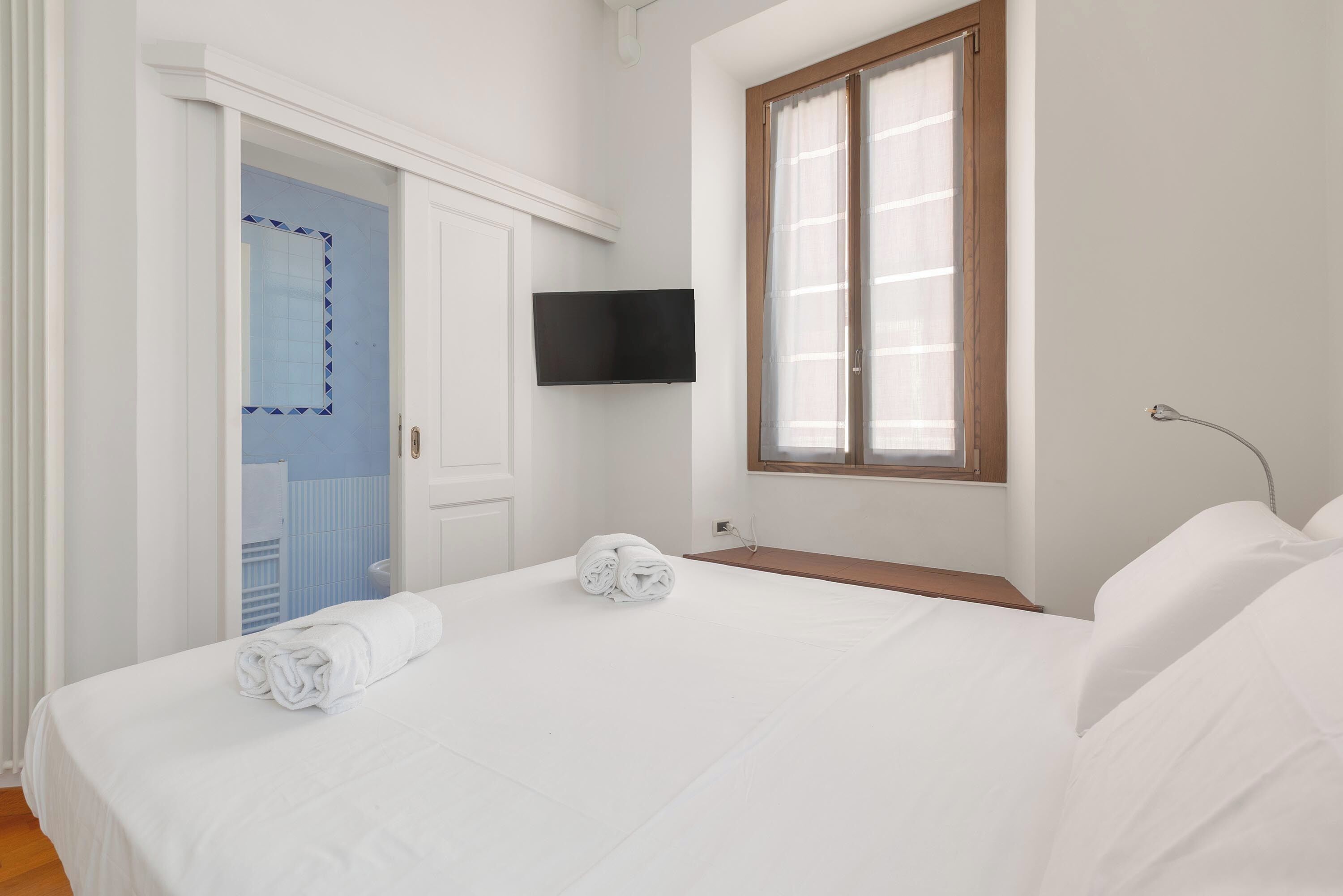 Una camera da letto con un letto, una televisione a muro e una finestra con tende.