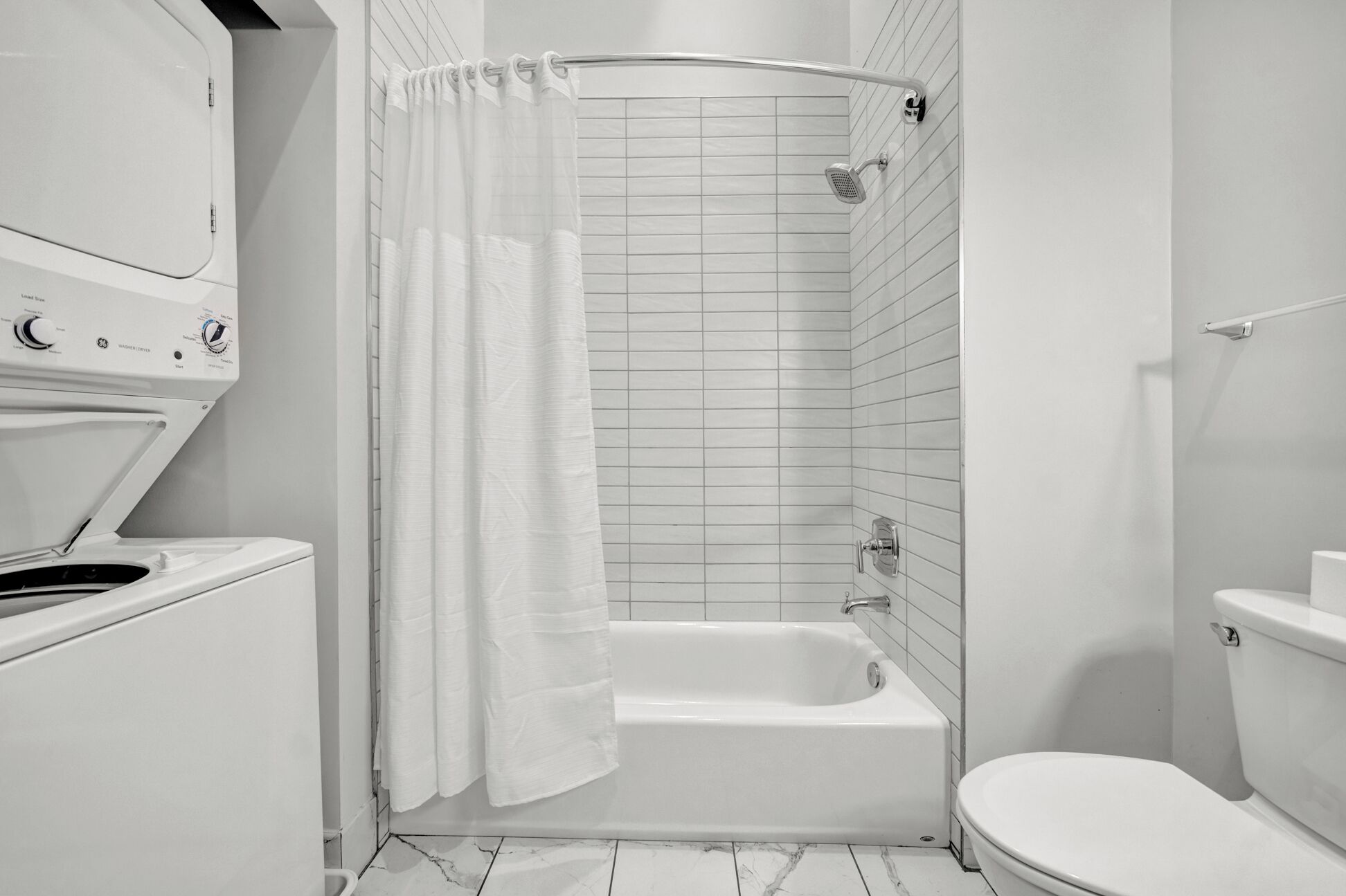 A bathroom with a white bathtub, a shower curtain, a toilet, and a washing machine.