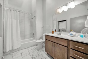 Une salle de bain moderne comprenant une baignoire, des toilettes, un meuble-lavabo avec un miroir et un espace douche.