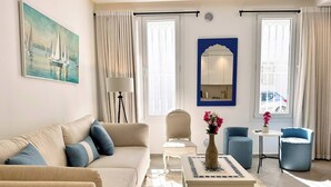 Uma sala de estar com sofá, cadeiras, uma mesinha, um vaso com flores, um quadro e uma janela com cortinas.