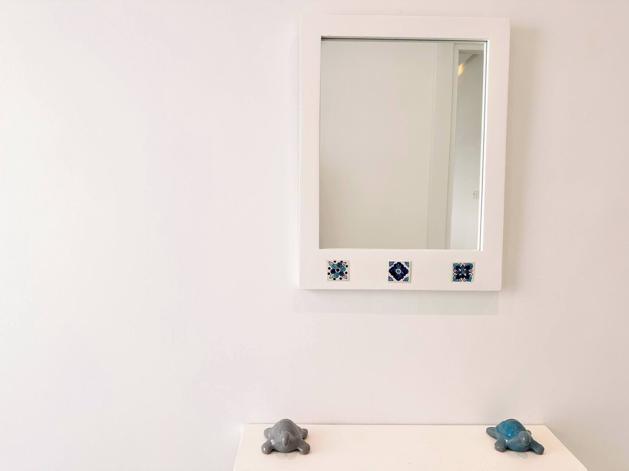 A white wall with a framed mirror and two small turtle figurines on a white surface below.