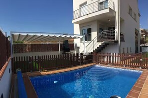 Ein Pool mit Holzterrasse, einer überdachten Sitzecke und einer Treppe, die zu einer erhöhten Ebene führt.