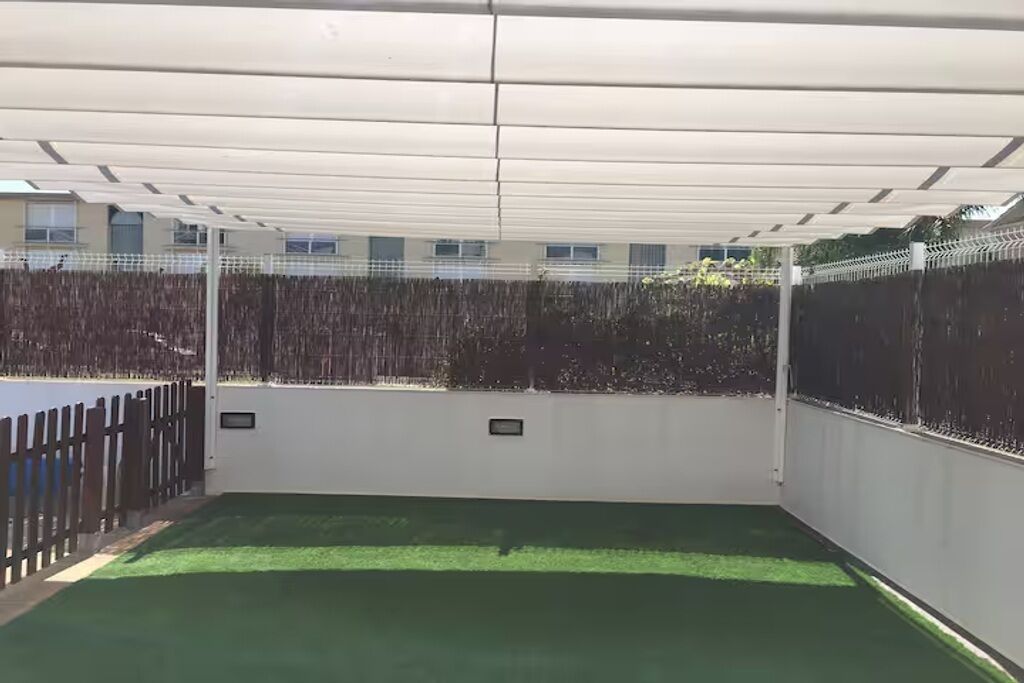 Un espacio exterior cubierto con césped artificial, una valla de madera y una pared blanca con dos placas pequeñas.