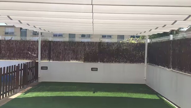 Uma área externa coberta com grama sintética, cerca de madeira e uma parede branca com duas pequenas placas.