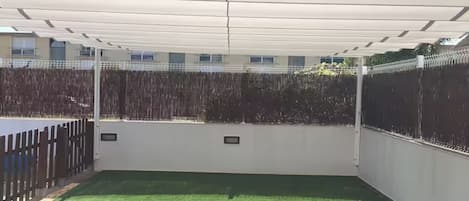 Un espacio exterior cubierto con césped artificial, una valla de madera y una pared blanca con dos placas pequeñas.