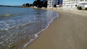 Uma praia com areal, mar calmo e uma fileira de edifícios brancos com varandas.